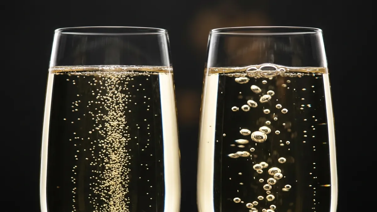 An extreme macro close-up of two sparkling wine glasses side by side: the left showing a fine, dense column of tiny rising bubbles, the right showing larger, sparser bubbles, illustrating the difference between bottle and tank fermentation