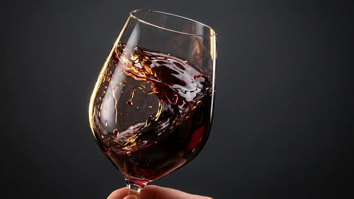A hand swirling a glass of red wine on a wooden bar counter