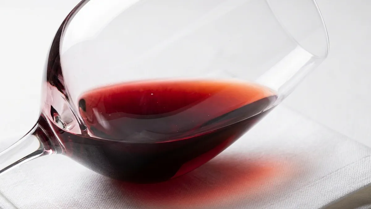 A wine glass tilted at a precise 45-degree angle against a white surface, showing the color gradient at the meniscus from deep ruby in the bowl to a pale orange-pink crescent at the rim