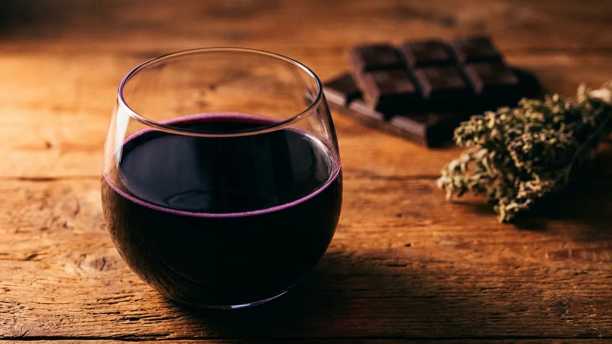 Inky purple-black Sagrantino wine in a glass on a rustic Umbrian wooden table with dark chocolate and dried herbs nearby