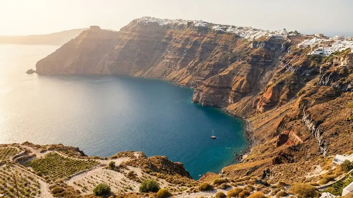 Aerial view of Santorini's blue Aegean caldera with whitewashed villages above dark volcanic cliffs and terraced vineyards below