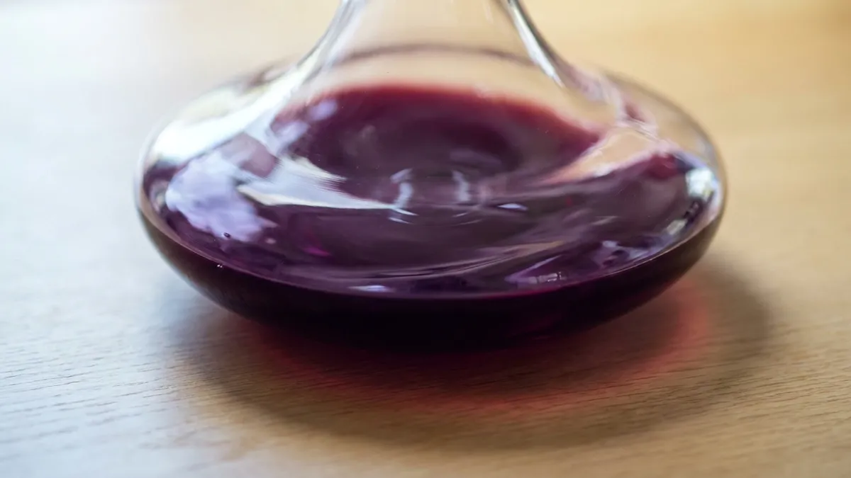 A young, deeply saturated purple-red wine swirling in a wide crystal decanter, its surface catching soft daylight and showing gentle motion as air meets the wine