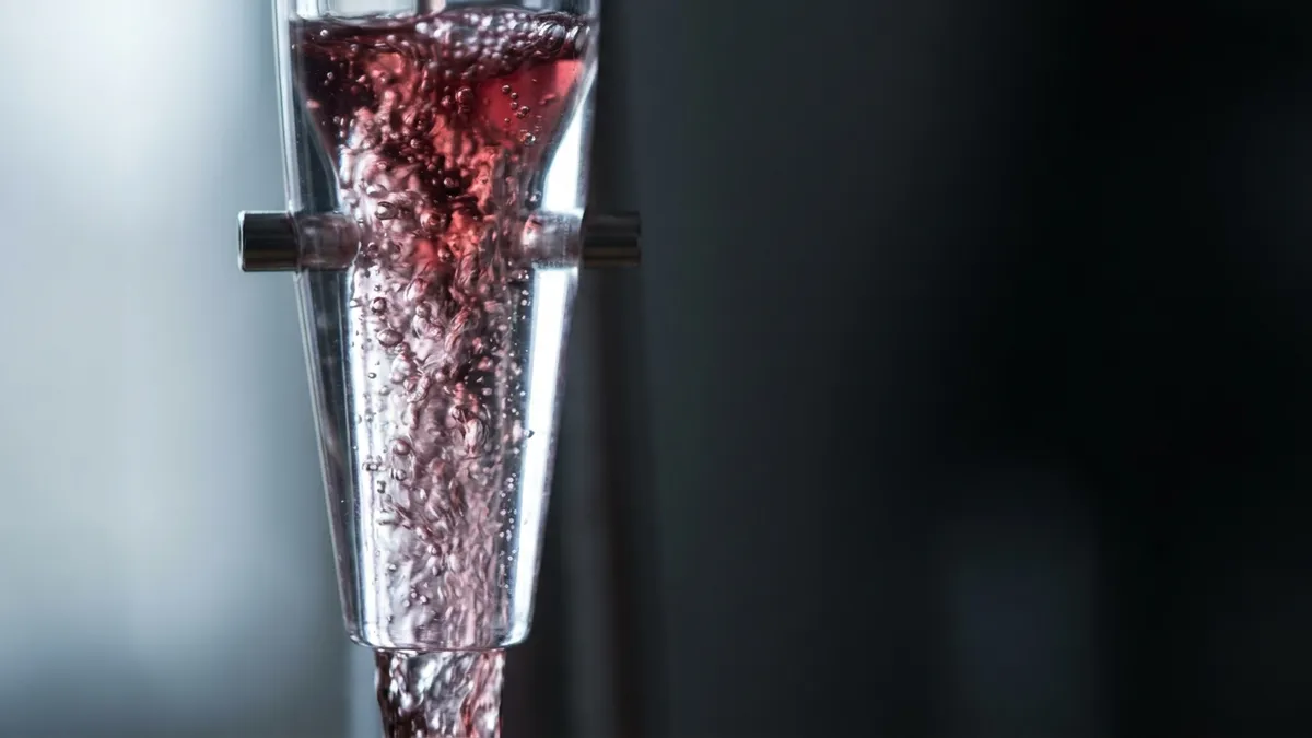 A close-up of red wine flowing through an aerator's air ports, the stream churning into fine bubbles against warm backlight