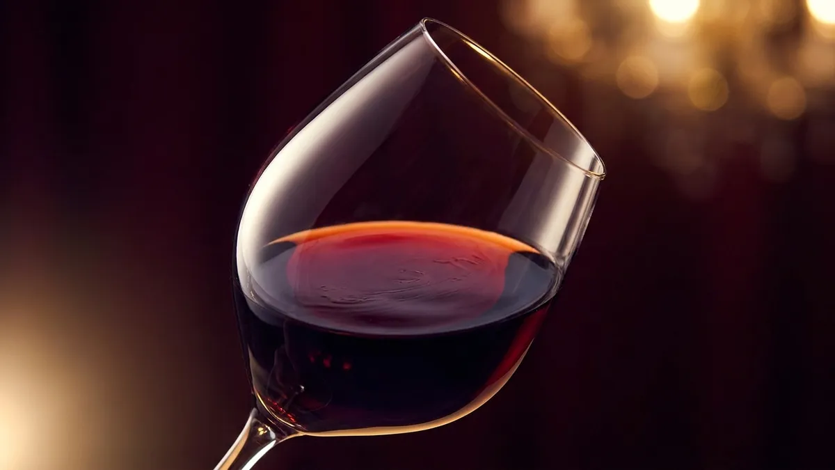 A wine glass held in soft light showing ruby wine with multiple overlapping reflections