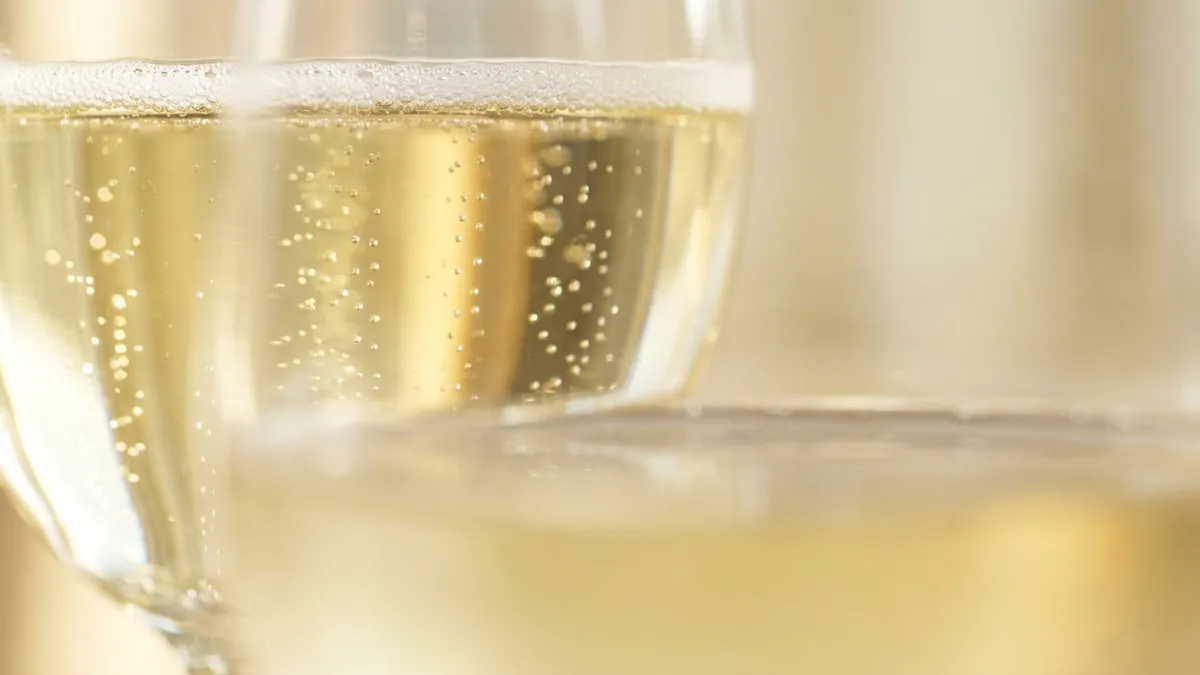 Fine bubbles rising in strings through a glass of pale gold sparkling wine in morning light