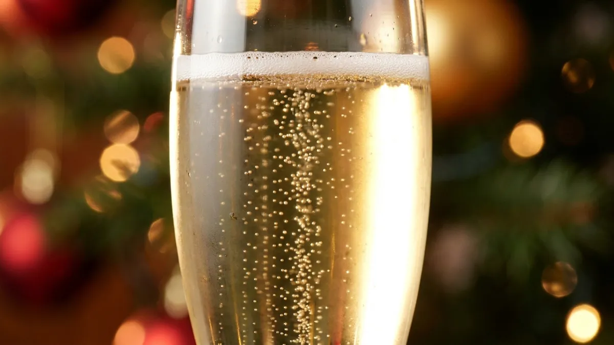 Fine streams of bubbles rising in a flute of pale gold sparkling wine against festive lights