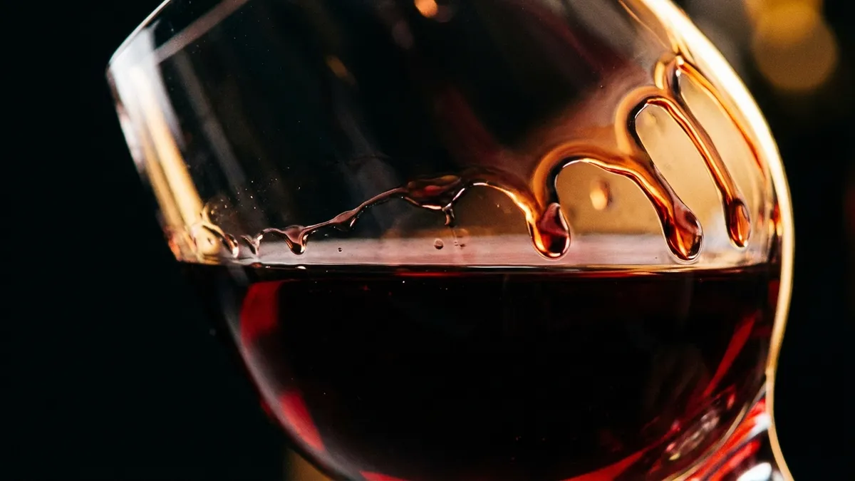 An extreme close-up of the inside of a tilted wine glass showing thick, slow-moving wine legs sliding down the glass wall in warm side lighting