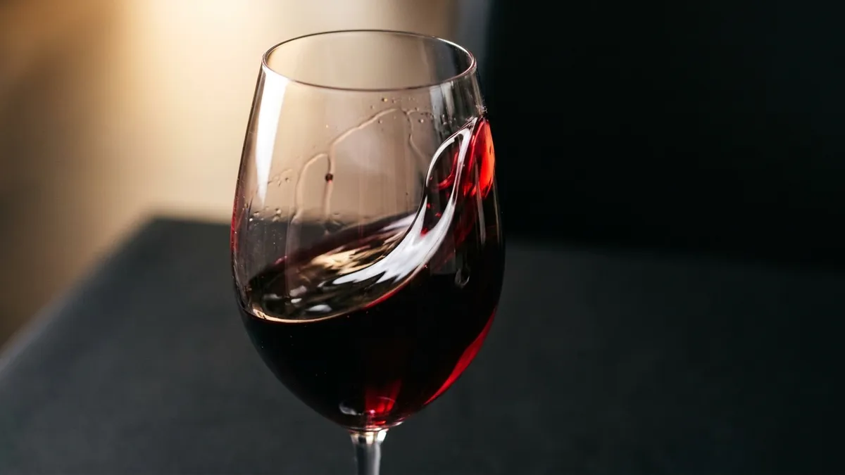 A glass of red wine mid-swirl on a plain dark surface, catching a shaft of warm light